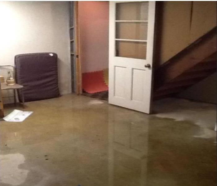 water pooling on concrete floor in a basement, door and stairway visible